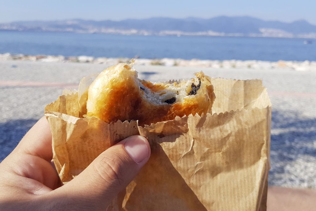 Holding a boyoz pastry while overlooking the beach.